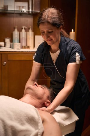 Téléchargez les photos : Ostéopathe féminin expérimenté étirant le cou de l'homme caucasien adulte pendant la séance d'ostéopathie - en image libre de droit