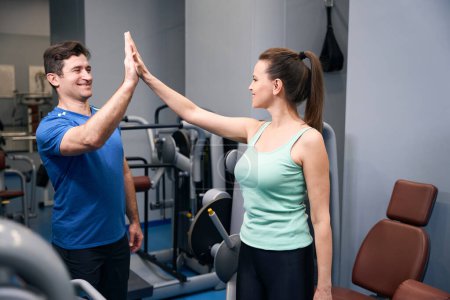 Téléchargez les photos : Femme en forme souriante donnant cinq à son entraîneur personnel heureux à la salle de gym - en image libre de droit