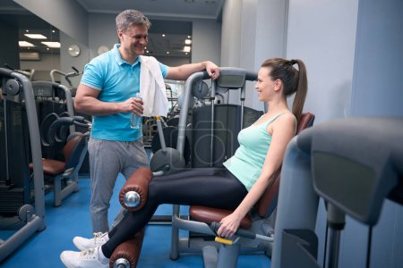 Photo for Cheerful fit lady working out on leg extension machine while talking to joyous fitness partner - Royalty Free Image