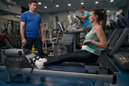 Photo for Serious sporty female working out on seated row machine under guidance of personal trainer - Royalty Free Image