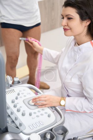 Photo for Doctor controls equipment and looking at monitor during diagnosis of patient lower extremities in the clinic - Royalty Free Image