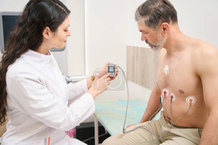 Foto de Médico joven que presenta indicaciones de trabajo del sistema cardiovascular al hombre en el hospital - Imagen libre de derechos