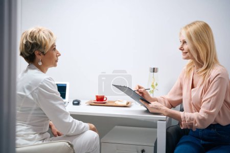 Foto de Mujer agradable rellena un cuestionario en una cita con un ginecólogo en un centro de cosmetología - Imagen libre de derechos