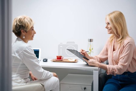 Foto de Mujer bonita rellena cuestionario médico en una cita con un ginecólogo en el centro de cosmetología - Imagen libre de derechos