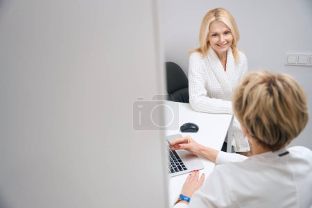 Foto de La dama sonriente escucha atentamente al ginecólogo en el centro de cosmetología. Mujer consultando en una cita con el médico - Imagen libre de derechos