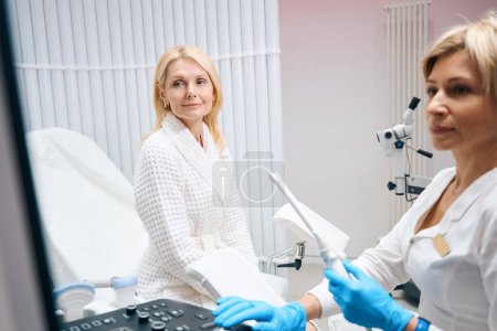Foto de El médico ginecólogo dice que el resultado del examen de ultrasonido a la paciente mujer. Ginecólogo habla con paciente con dispositivo de ultrasonido en las manos - Imagen libre de derechos