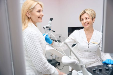Foto de Mujer paciente y médico ginecólogo sonríen juntos durante un examen por ultrasonido de las glándulas mamarias - Imagen libre de derechos