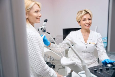Foto de Ginecóloga femenina y su paciente sonríen juntas durante el procedimiento para diagnosticar glándulas mamarias mediante ultrasonido - Imagen libre de derechos