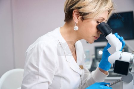 Photo for Close up photo of a gynecologist woman who carefully looks through the eyepieces of a microscope - Royalty Free Image