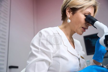 Téléchargez les photos : Photo recadrée d'une gynécologue féminine qui se concentre sur l'étude du matériau à travers un microscope - en image libre de droit
