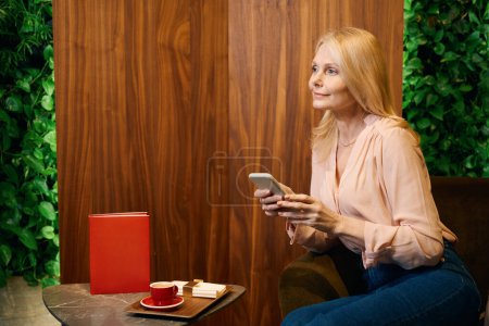Téléchargez les photos : Dame heureuse avec smartphone dans ses mains assis dans un salon de beauté à la table de bijoux - en image libre de droit