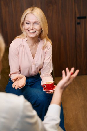 Téléchargez les photos : Photo verticale recadrée de dame heureuse avec tasse de café qui a une conversation amusante avec le médecin dans le salon de spa - en image libre de droit