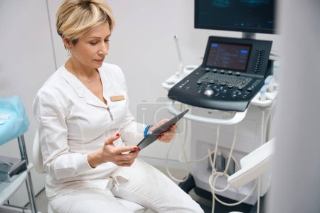 Foto de Foto de una ginecóloga mirando una tableta sobre el fondo de un dispositivo de ultrasonido - Imagen libre de derechos