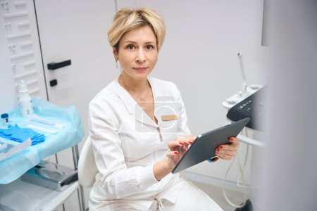 Foto de Retrato de una ginecóloga usando tableta en su consultorio. Médico en proceso de trabajo utiliza gadget - Imagen libre de derechos