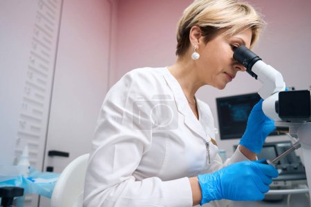Photo for Focused female gynecologist carefully examines samples of analysis through microscope. Doctor gynecologist concentrated uses microscope - Royalty Free Image
