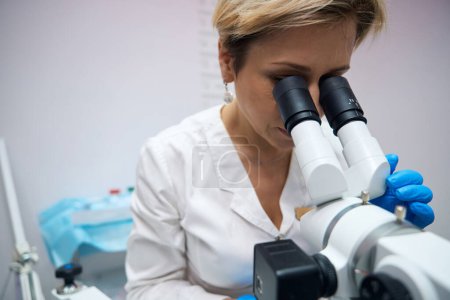Téléchargez les photos : Photo d'une gynécologue féminine concentrée qui travaille soigneusement au microscope. Le médecin gynécologue examine attentivement le microscope - en image libre de droit