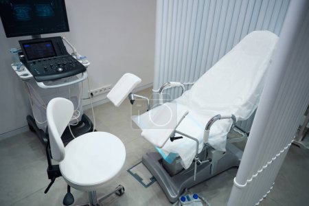 Téléchargez les photos : Photo du bureau du gynécologue qui abrite l'équipement pour l'examen des patients. Office pour recevoir des patients avec chaise gynécologique et échographe - en image libre de droit