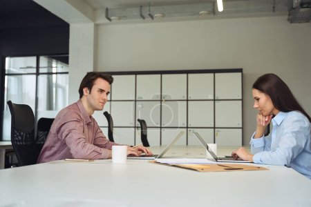 Téléchargez les photos : Travailleur d'entreprise pensif et son collègue concentré assis au bureau devant les ordinateurs - en image libre de droit