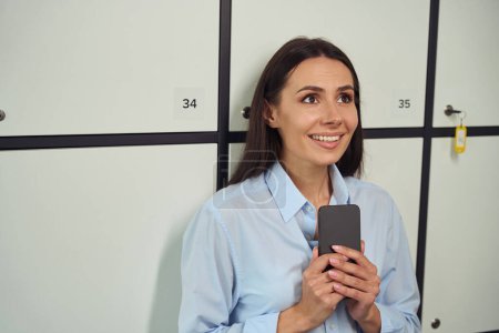 Foto de Retrato de la joven alegre con el teléfono celular apoyado contra el armario de almacenamiento - Imagen libre de derechos