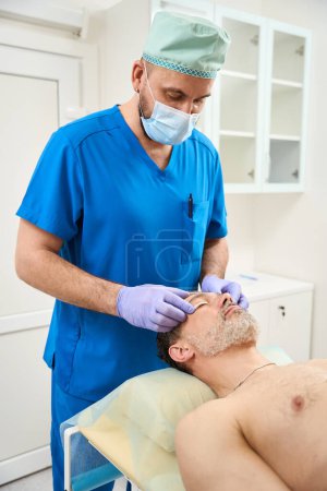 Foto de Doctor en una máscara pega parches en los párpados de un cliente masculino. Cirugía plástica - Imagen libre de derechos