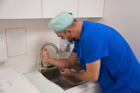 Téléchargez les photos : Le docteur en costume bleu se lave les mains après l'opération. Vue latérale - en image libre de droit