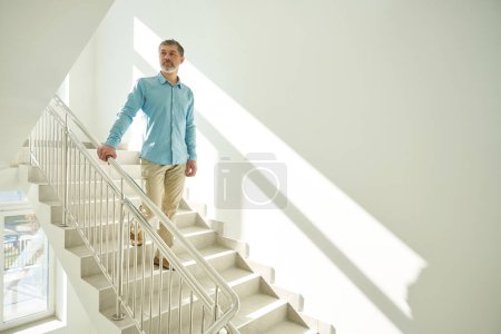 Photo for Handsome male holding the handrails goes down the steps of the medical clinic with a white interior - Royalty Free Image