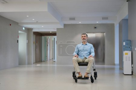 Photo for Portrait of adult sitting man in a wheelchair in the corridor of a modern medical clinic - Royalty Free Image