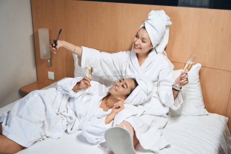 Foto de Damas felices en la habitación del hotel descansan en la cama. Las amigas se divierten celebrando un viaje en un viaje - Imagen libre de derechos