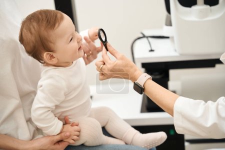 Téléchargez les photos : Ophtalmologiste main tenant loupe devant le visage du bébé en présence des parents - en image libre de droit