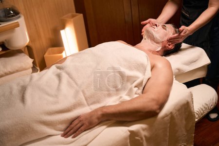 Photo for Cropped photo of female cosmetician placing sheet mask over male client face - Royalty Free Image