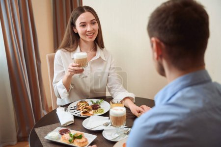 Photo for Young guy and lady having breakfast sitting at the table in a bright hotel. Check-in hotel - Royalty Free Image