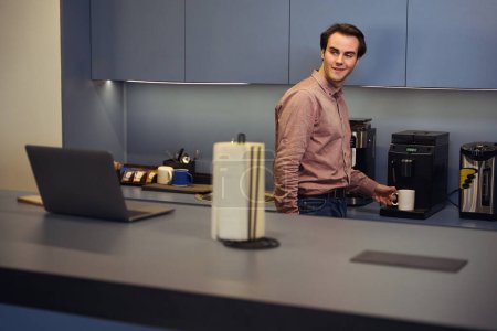 Téléchargez les photos : Employé de l'entreprise agréable regardant le moniteur d'ordinateur tout en mettant tasse sur plateau goutte à goutte machine à café - en image libre de droit