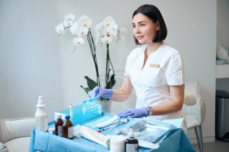 Photo for Doctor in gloves sitting at cosmetology office in front of medical stuff on desk - Royalty Free Image