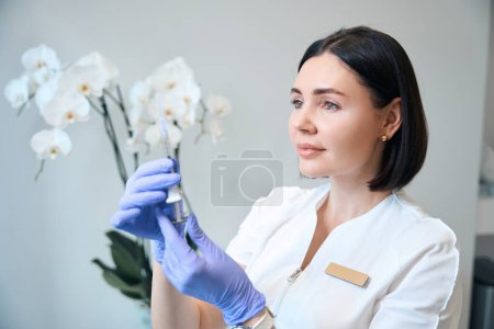 Téléchargez les photos : Esthéticienne médicale tenant une seringue injectable et portant des gants dans un salon de beauté - en image libre de droit