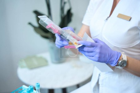 Téléchargez les photos : Gros plan des mains du cosmétologue médical dans des gants tenant l'emballage avec une seringue - en image libre de droit