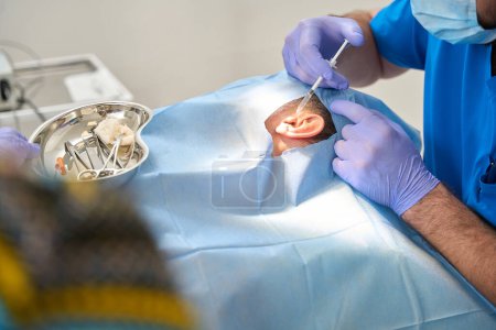 Téléchargez les photos : Homme âgé patient allongé sur la table d'opération est injecté dans son oreille pendant l'opération - en image libre de droit