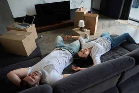 Téléchargez les photos : Couple se couche sur le canapé dans leur nouvel appartement après avoir emménagé. - en image libre de droit