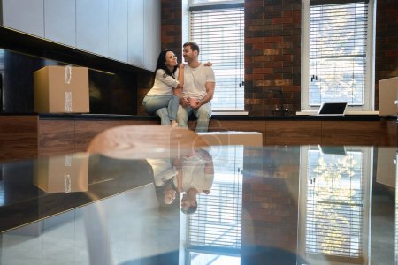 Téléchargez les photos : Homme et femme en t-shirts blancs sont assis sur la table de nuit dans la nouvelle cuisine - en image libre de droit