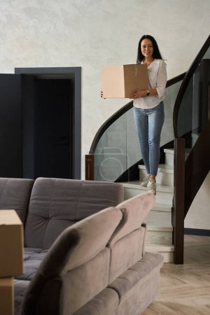 Photo for Brunette woman stands with a box on the stairs in the house - Royalty Free Image