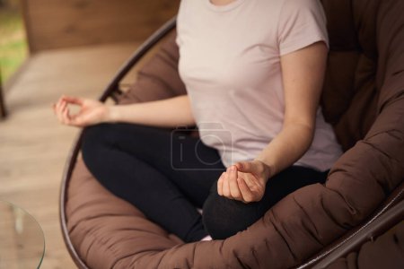 Photo for Young woman sitting in lotus position on armchair near desk, resting in the morning - Royalty Free Image