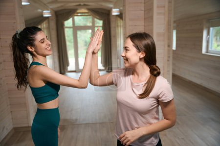Photo for Happy women standing on the room and high five, looking at each other - Royalty Free Image