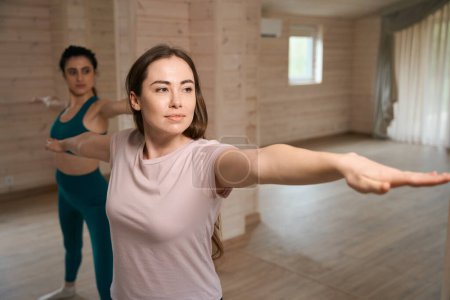 Photo for Young women in tracksuits standing near each other and balance exercise at home - Royalty Free Image