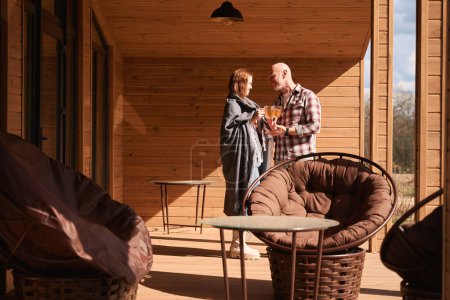 Foto de Cuidar esposa sirviendo bebida herbal a su marido feliz en la terraza de la casa de campo - Imagen libre de derechos