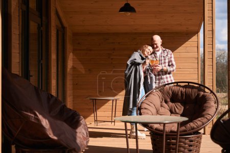 Téléchargez les photos : Femme attentionnée servant une boisson aux herbes à son mari heureux sur la terrasse de la maison de campagne - en image libre de droit