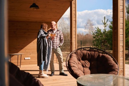 Téléchargez les photos : Couple romantique claquant leurs tasses en verre tout en se tenant debout sur la terrasse de la maison de campagne - en image libre de droit