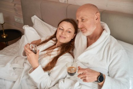 Téléchargez les photos : Couple marié rêvant au lit avec des tasses de café dans leurs mains - en image libre de droit