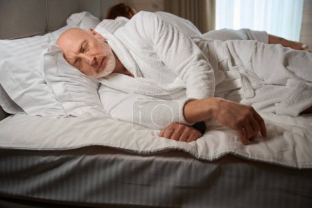 Foto de Tranquilo hombre en albornoz dormitando en la acogedora cama junto a su esposa - Imagen libre de derechos