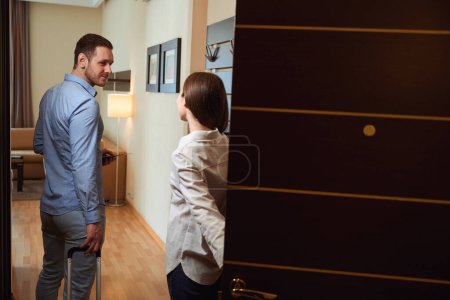Téléchargez les photos : Homme et femme se tiennent à la porte ouverte de la chambre d'hôtel dans laquelle ils séjournent - en image libre de droit