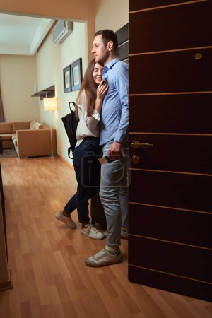 Foto de Atractiva jovencita abrazando a un hombre cerca de la puerta de la habitación del hotel. Check in hotel - Imagen libre de derechos