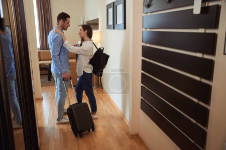 Photo for Young lady put her hands on the shoulders of a man with a suitcase in a hotel room - Royalty Free Image